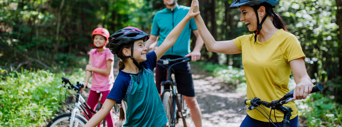 A young family with little children preapring for bike ride, standing with bicycles in nature and high fiving.