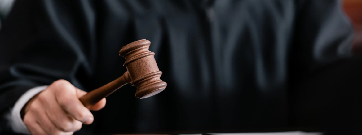 Header - Courtroom partial view of blurred judge in robe holding gavel in court