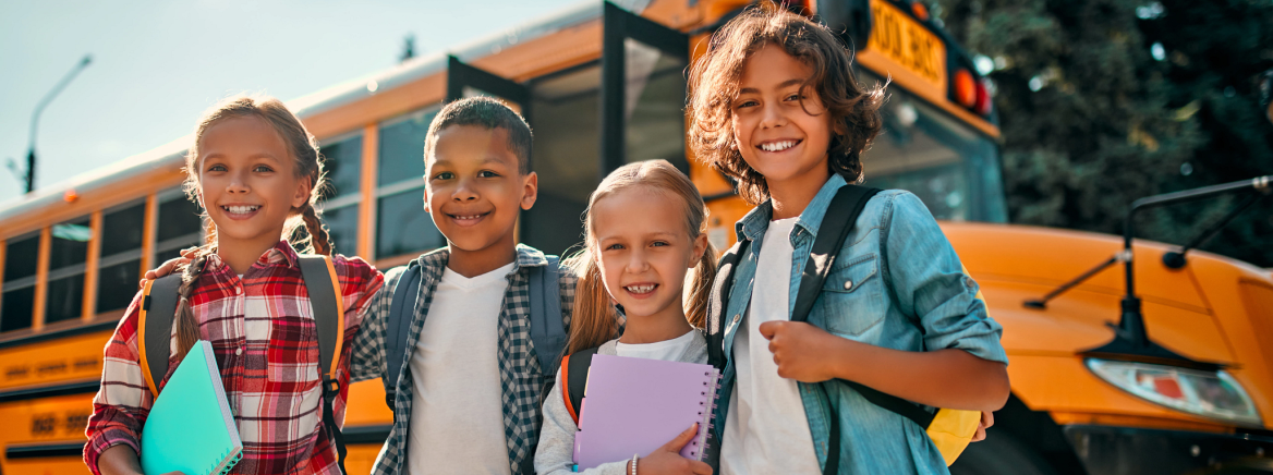 Kids by School Bus Back to school. Multiracial pupils of primary school near school bus. Happy children ready to study.