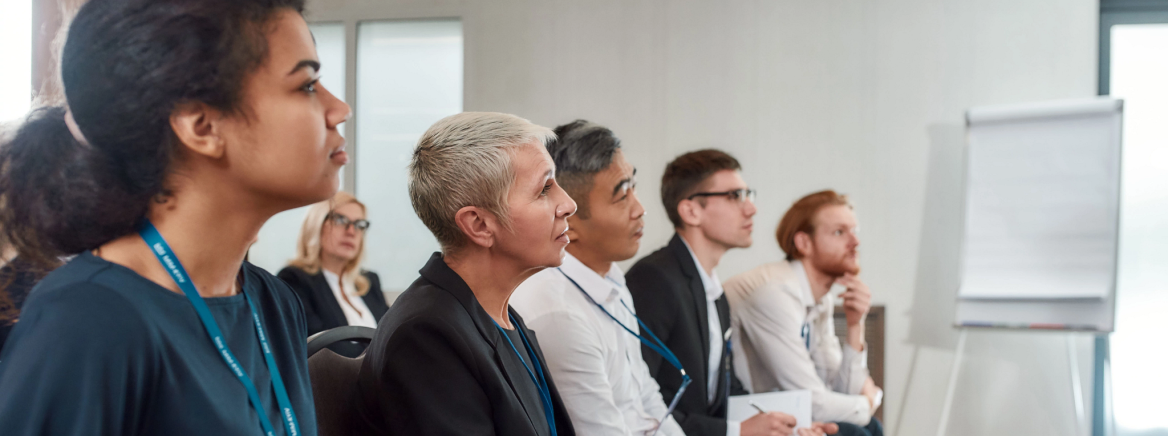 Get Together. Multi-ethnic audience sitting in a row while listening to presentation at conference hall Multi-ethnic audience sitting in a row and making notes while listening to presentation at conference hall. Selective focus. Horizontal shot. Side view