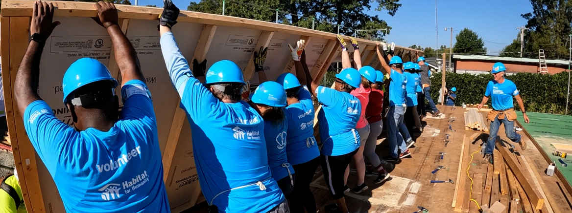 A group of volunteers hold of wood framework s a new house os constructed.