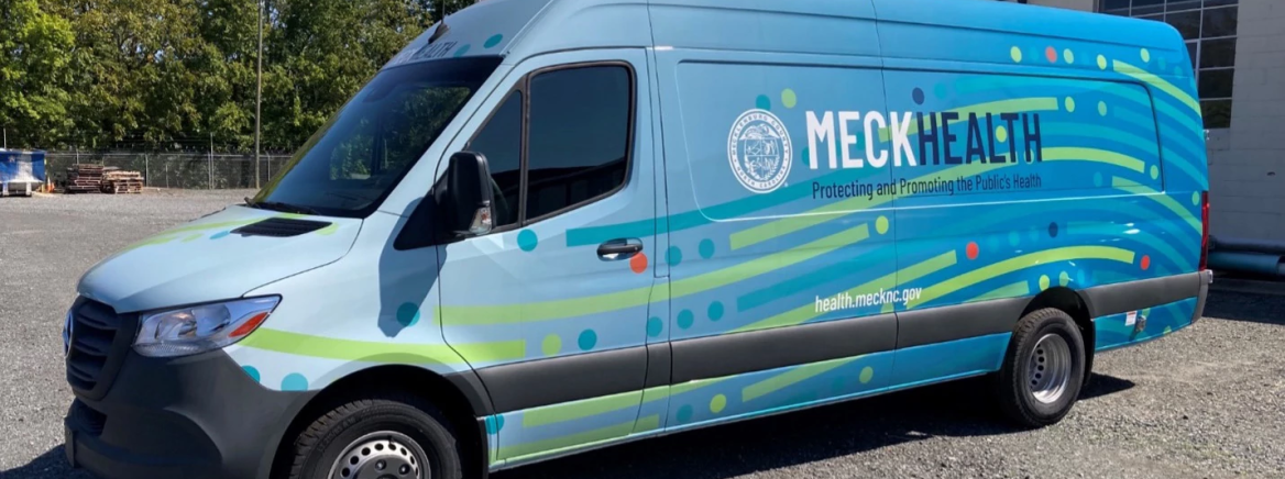 Side view of a light blue van with the County seal and the words Meck Health