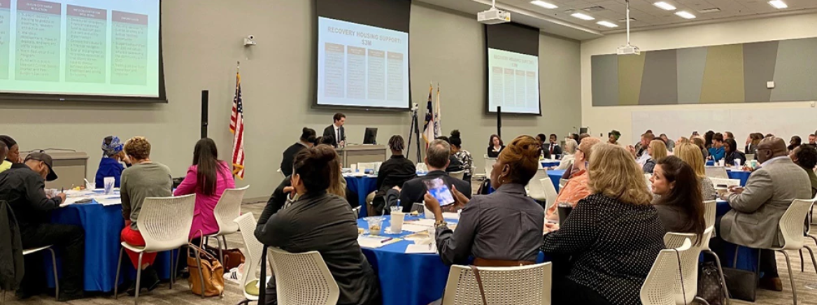 A group of community meetings sitting at tables in a large conference room