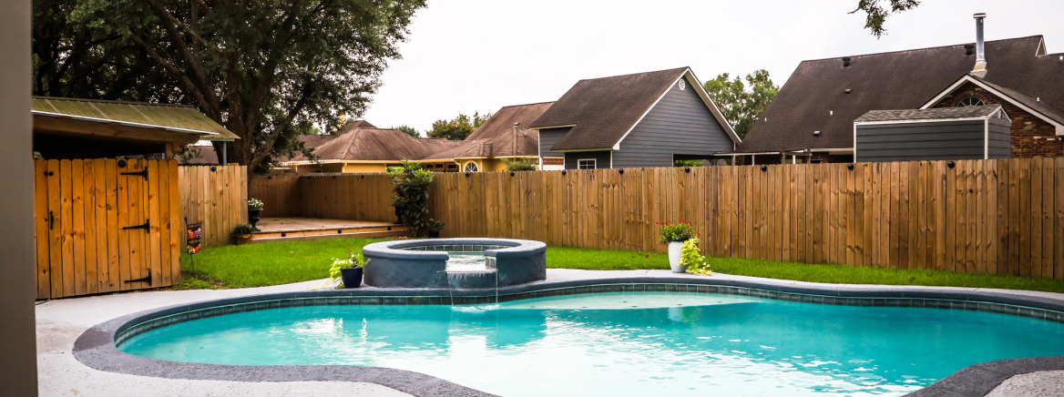 residential pool A large free form gray grey accent swimming pool with turquoise blue swim water in a fenced in backyard in a suburb neighborhood.