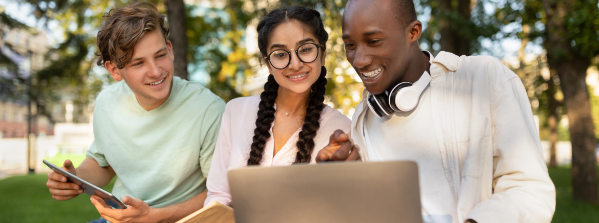 Studets using a computer in a park Group of students looking at a computer in a park