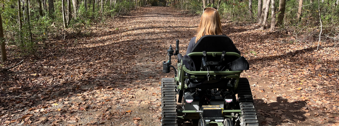 all terrain wheelchair A woman riding in an all terrain accessible wheelchair to explore a trail on a fall day.