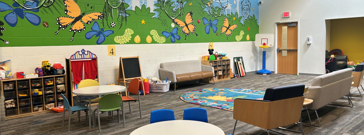 Mecklenburg County Community Support Services operates a Supervised Visitation and Safe Exchange Center (SVSE) specifically for families experiencing intimate partner violence.  The room features a table with blue chairs, sofas and a colorful mural on the wall.