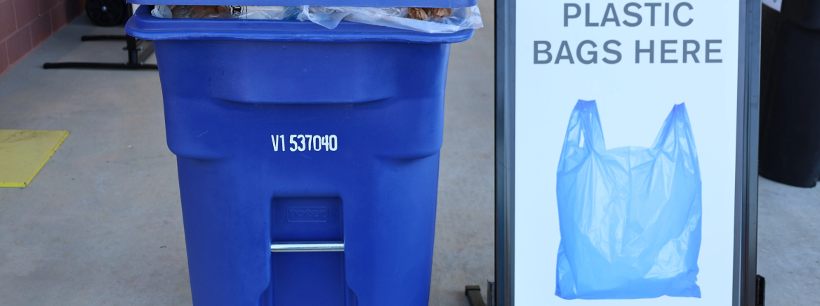 A blue bin next to a sign that says plastic bags here