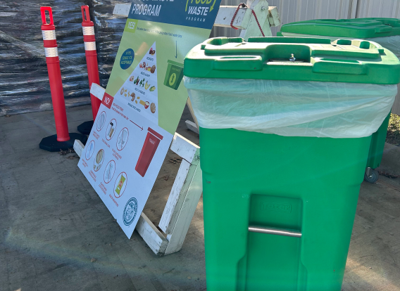 A green recycling bin to the right of a sign with the food pyramid
