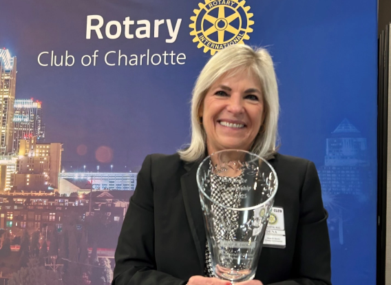County Manager Dena R. Diorio smiles while holding the Excellence in Leadership Award in front of a backdrop with the Charlotte skyline and the words Rotary Club of Charlotte. The award was presented to her by the Rotary Club of Charlotte on Feb. 11, 2025.