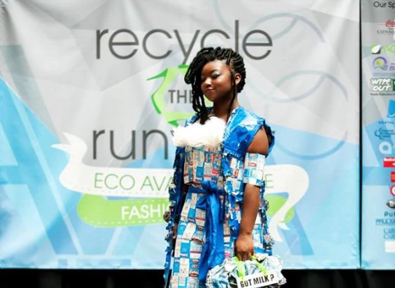 A teenager wearing a blue dress made up of repurposed cartoons and magazines walks the runway.