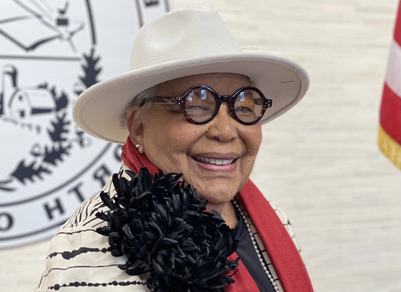 District Commissioner Vilma D. Leake standing in front of a wall with an American flag on the left and County seal on the right.